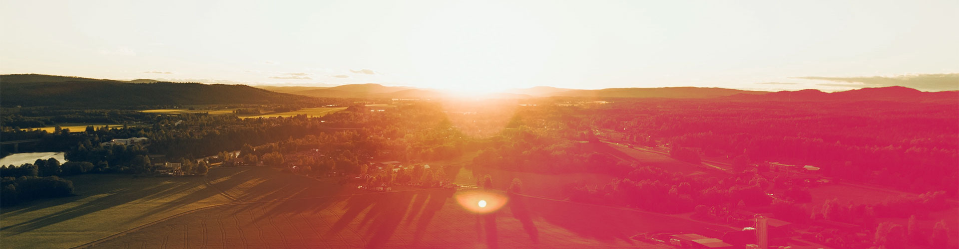 Dorf von oben inmitten von grünen Wiesen und Wäldern beim Sonnenuntergang